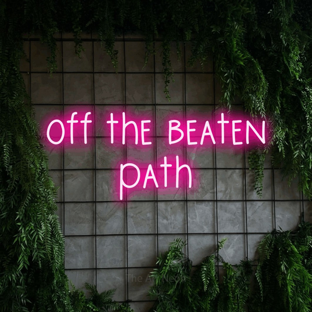 Hot pink LED neon sign reading "Off the Beaten Path" against a green grid wall with foliage