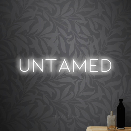 Cool white LED neon sign reading "Untamed" against light grey floral wallpaper
