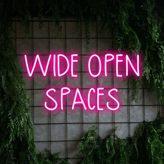 Hot pink LED neon sign reading "Wide Open Spaces" against a green grid wall with foliage