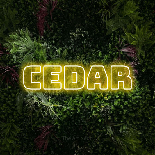 Yellow outline-style LED neon sign reading "Cedar" against a lush garden wall with pink flowers