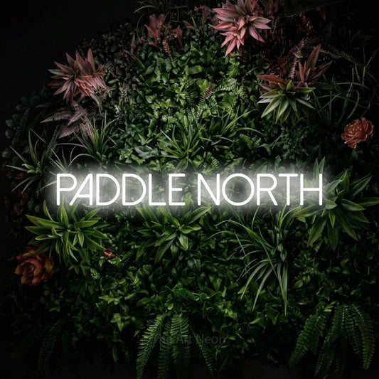 Cool white LED neon sign reading "Paddle North" against a flowering garden wall