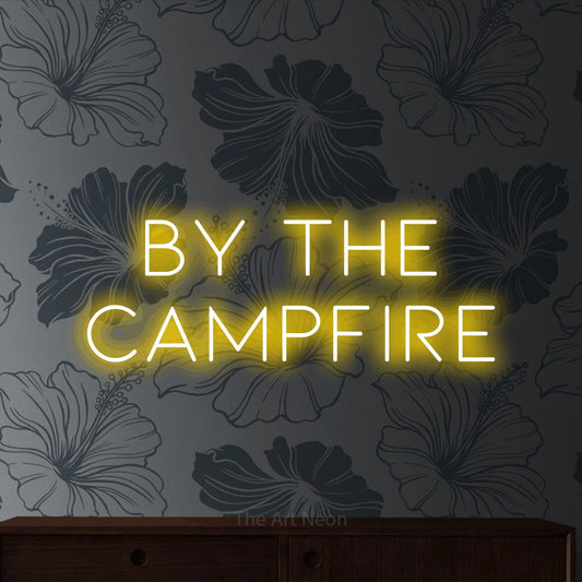Yellow LED neon sign reading "By the Campfire" against grey floral wallpaper