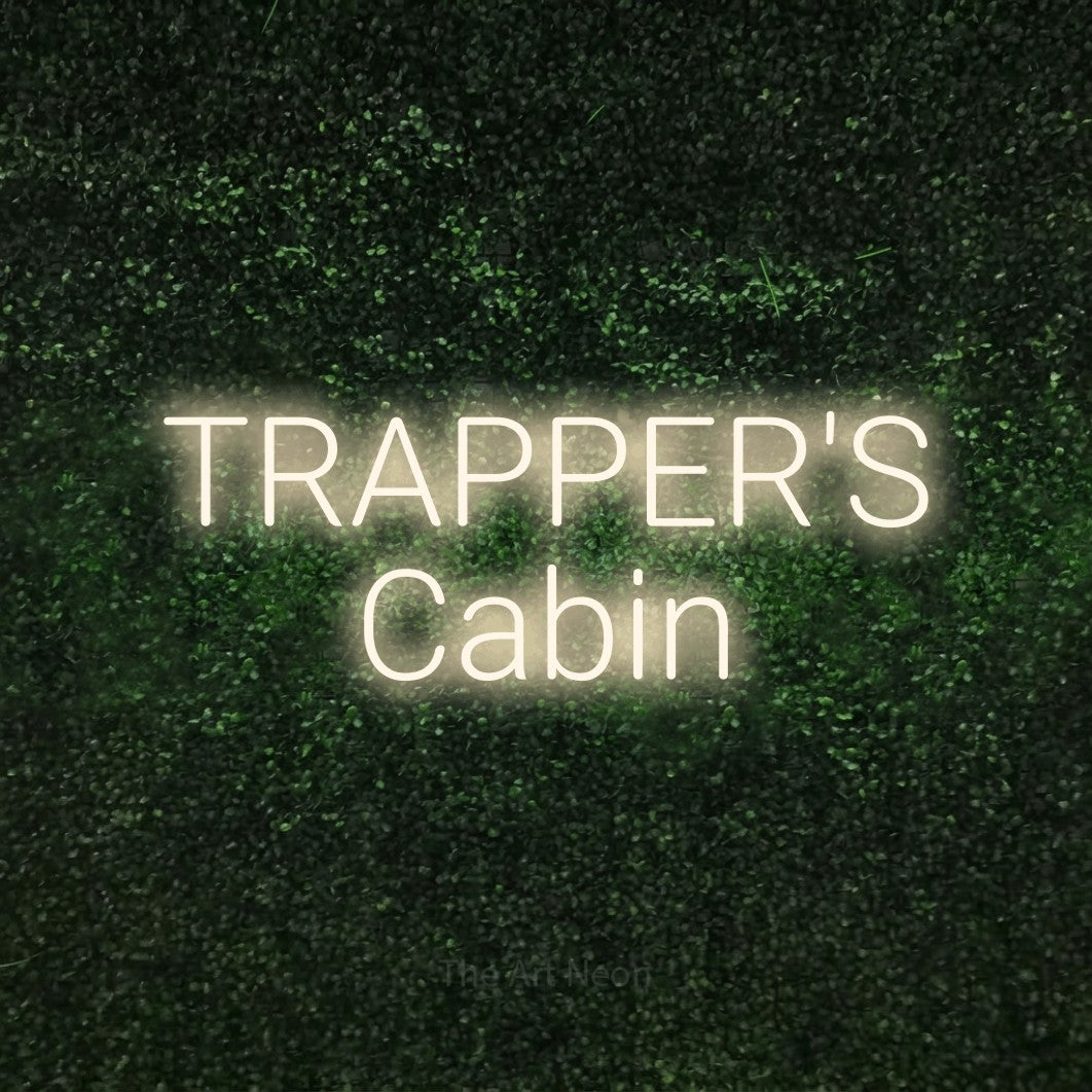 Warm white LED neon sign reading "Trapper's Cabin" against a textured green moss wall