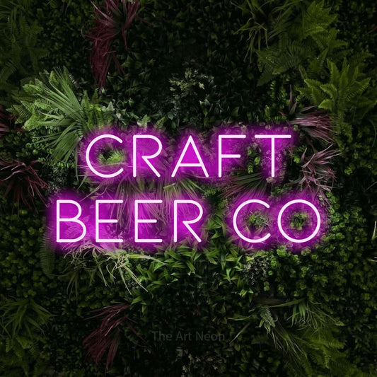 Pink LED neon sign reading "Craft Beer Co" against a lush garden wall with pink flowers