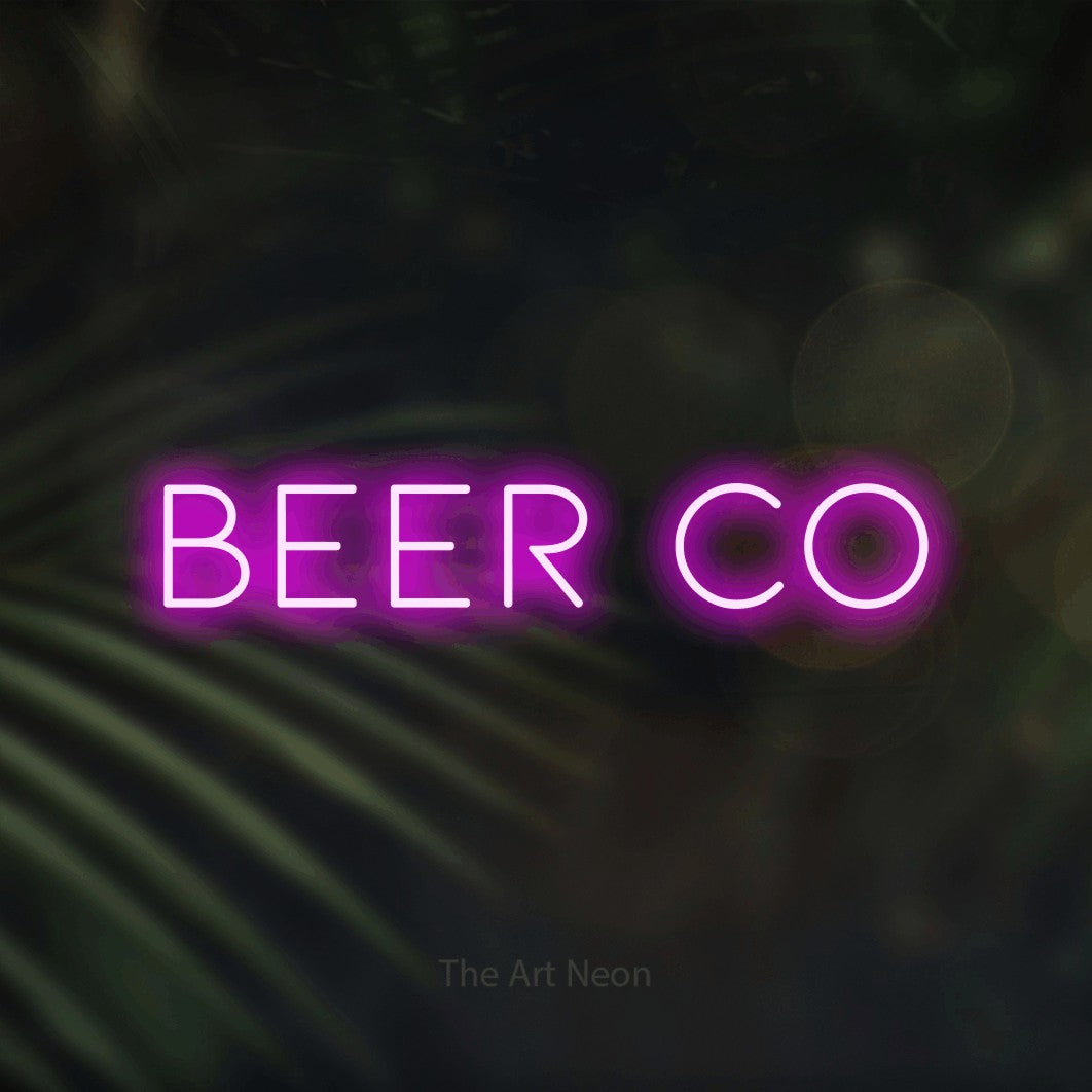 Pink LED neon sign reading "Beer Co" against dark blurred palm leaves