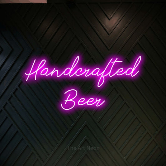 Pink script-style LED neon sign reading "Handcrafted Beer" against a dark geometric wood wall