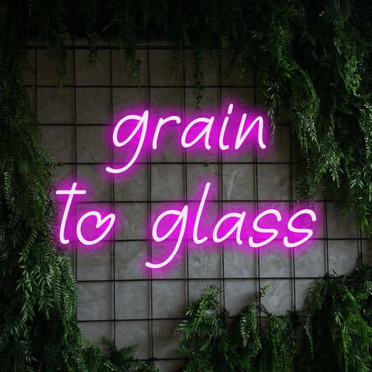 Pink LED neon sign reading "Grain to Glass" against a green grid wall with foliage