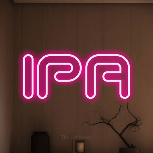 Hot pink outline-style LED neon sign reading "IPA" against a warm brown wall