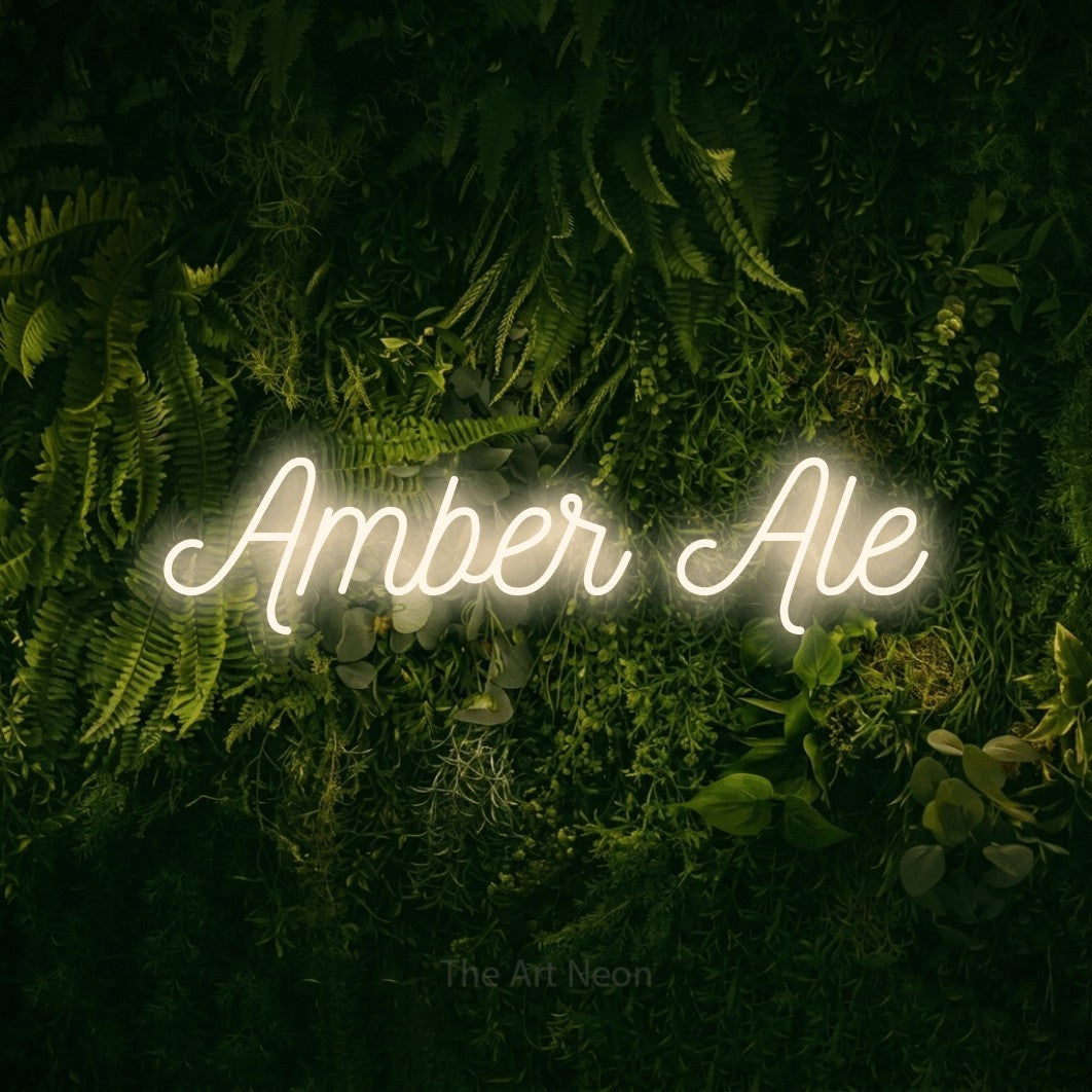 Warm white script-style LED neon sign reading "Amber Ale" against a moss-covered green wall