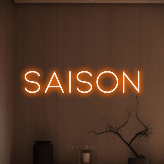 Orange LED neon sign reading "Saison" against a warm brown wall
