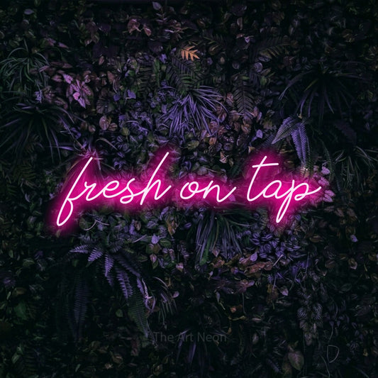 Hot pink script-style LED neon sign reading "Fresh on Tap" against a purple floral wall