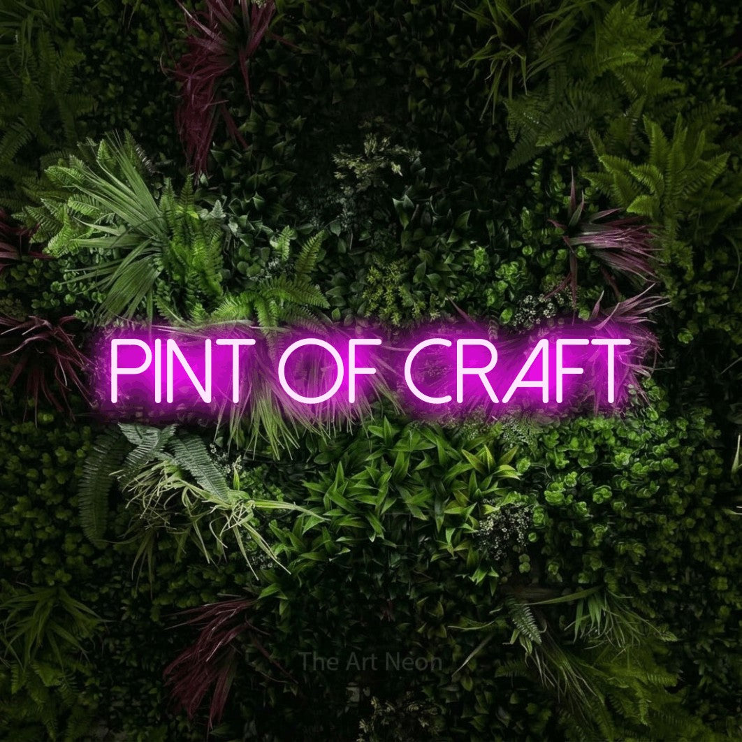 Pink LED neon sign reading "Pint of Craft" against a lush garden wall with pink flowers