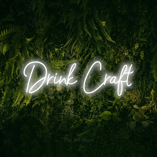 Cool white script-style LED neon sign reading "Drink Craft" against a moss-covered green wall
