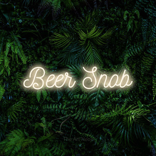 Warm white script-style LED neon sign reading "Beer Snob" against a dense tropical foliage wall