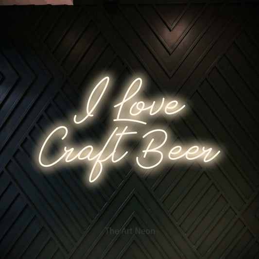 Warm white script-style LED neon sign reading "I Love Craft Beer" against a dark geometric wood wall