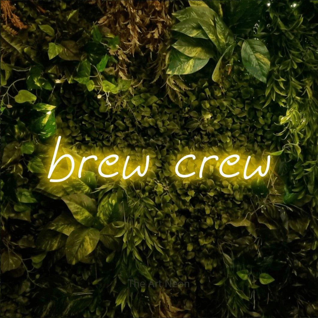 Yellow LED neon sign reading "Brew Crew" against a textured moss and foliage wall