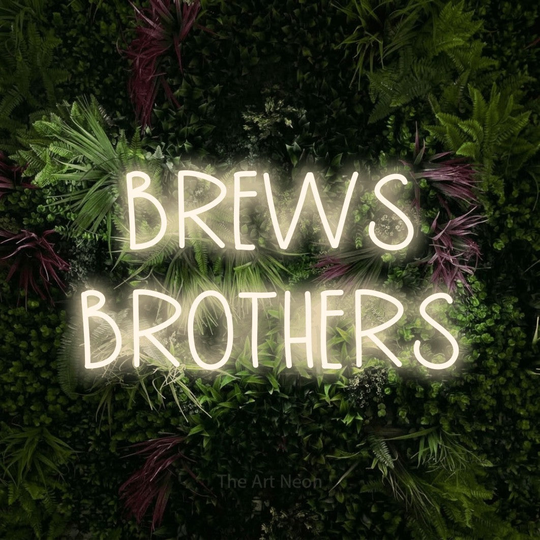 Warm white LED neon sign reading "Brews Brothers" against a lush garden wall with pink flowers