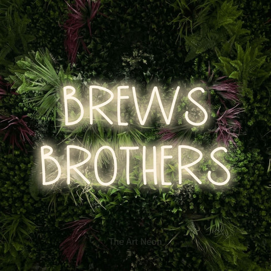 Warm white LED neon sign reading "Brews Brothers" against a lush garden wall with pink flowers