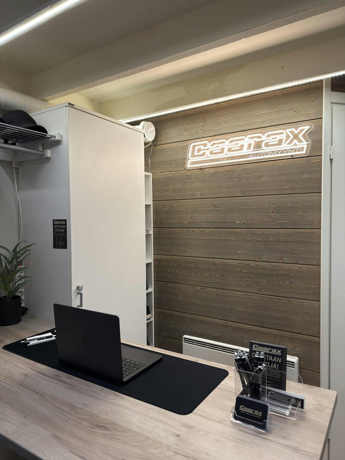 Warm-white Caarax Automyynti logo LED neon installed on a wood-panel office reception wall