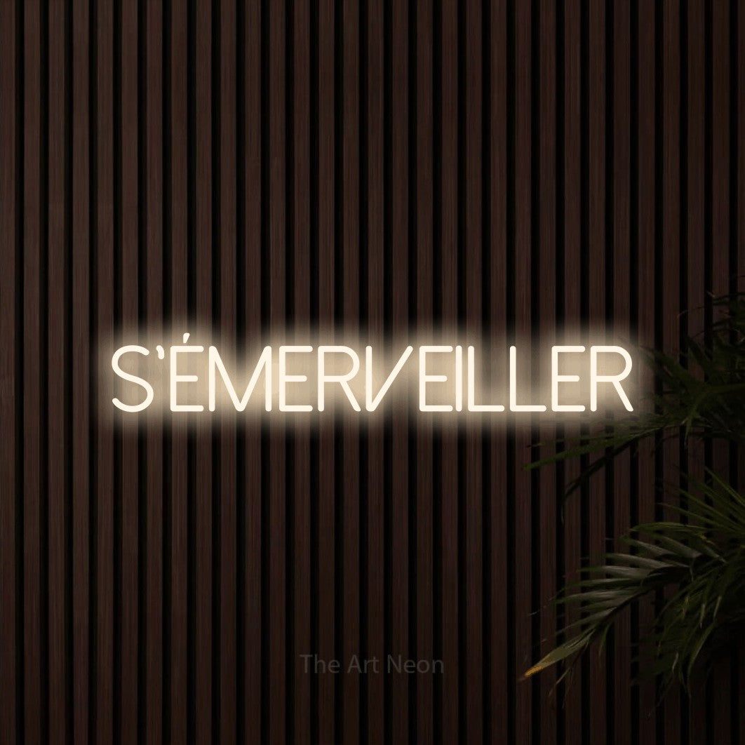 “S'émerveiller” LED neon sign in warm white, with thin sans-serif lettering, shown against dark wooden wall slats.