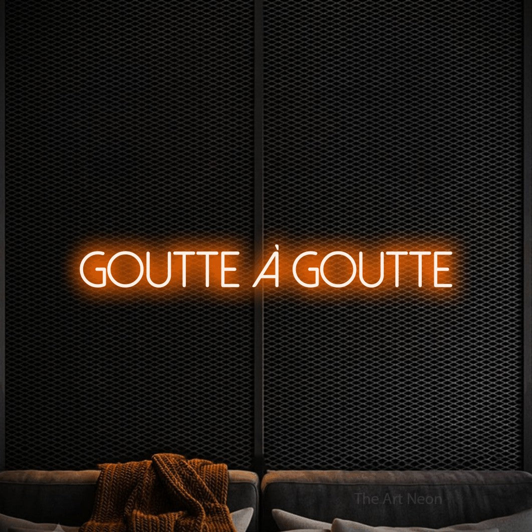 “Goutte à goutte” LED neon sign in orange, with thin sans-serif lettering, shown against a modern dark-toned seating area.