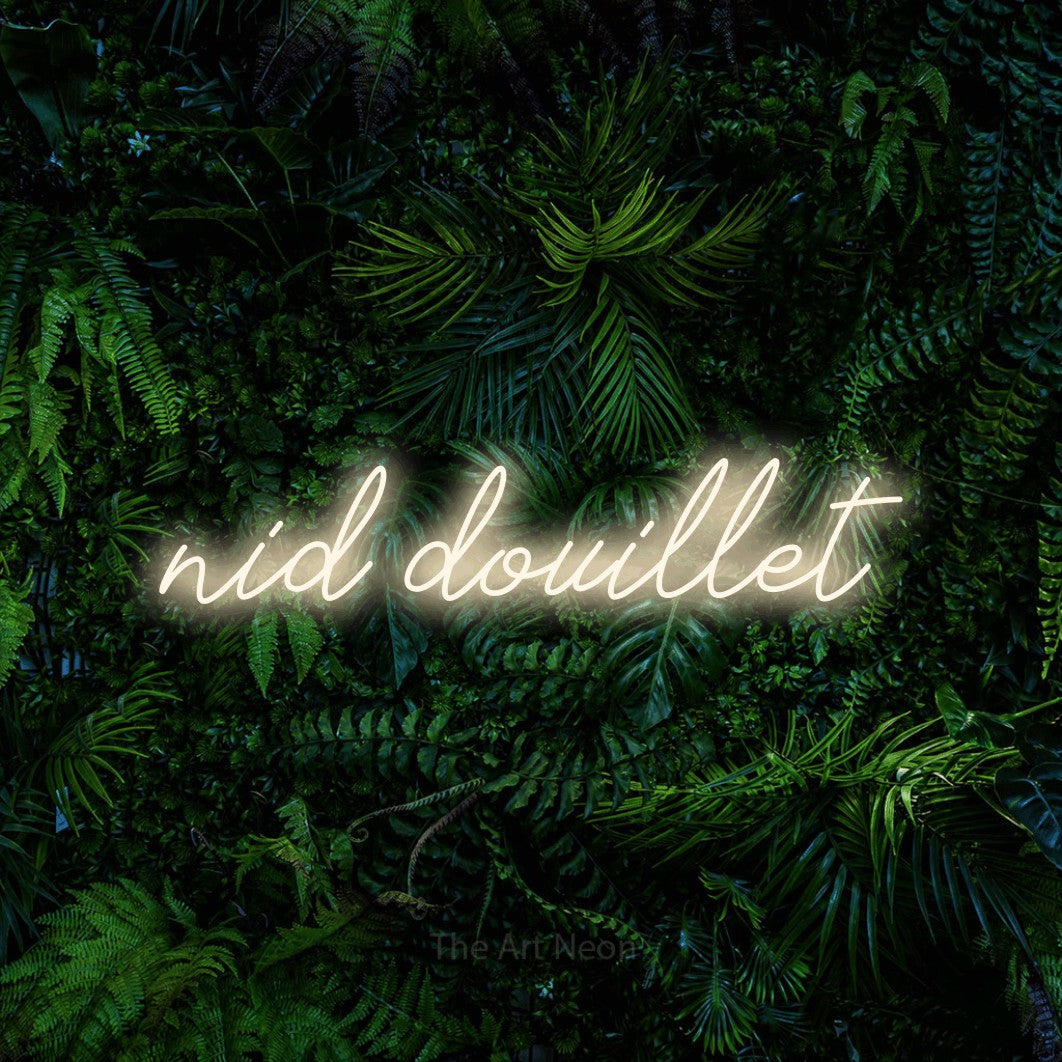 “Nid douillet” LED neon sign in warm white, with cursive lettering, shown against dense tropical foliage.