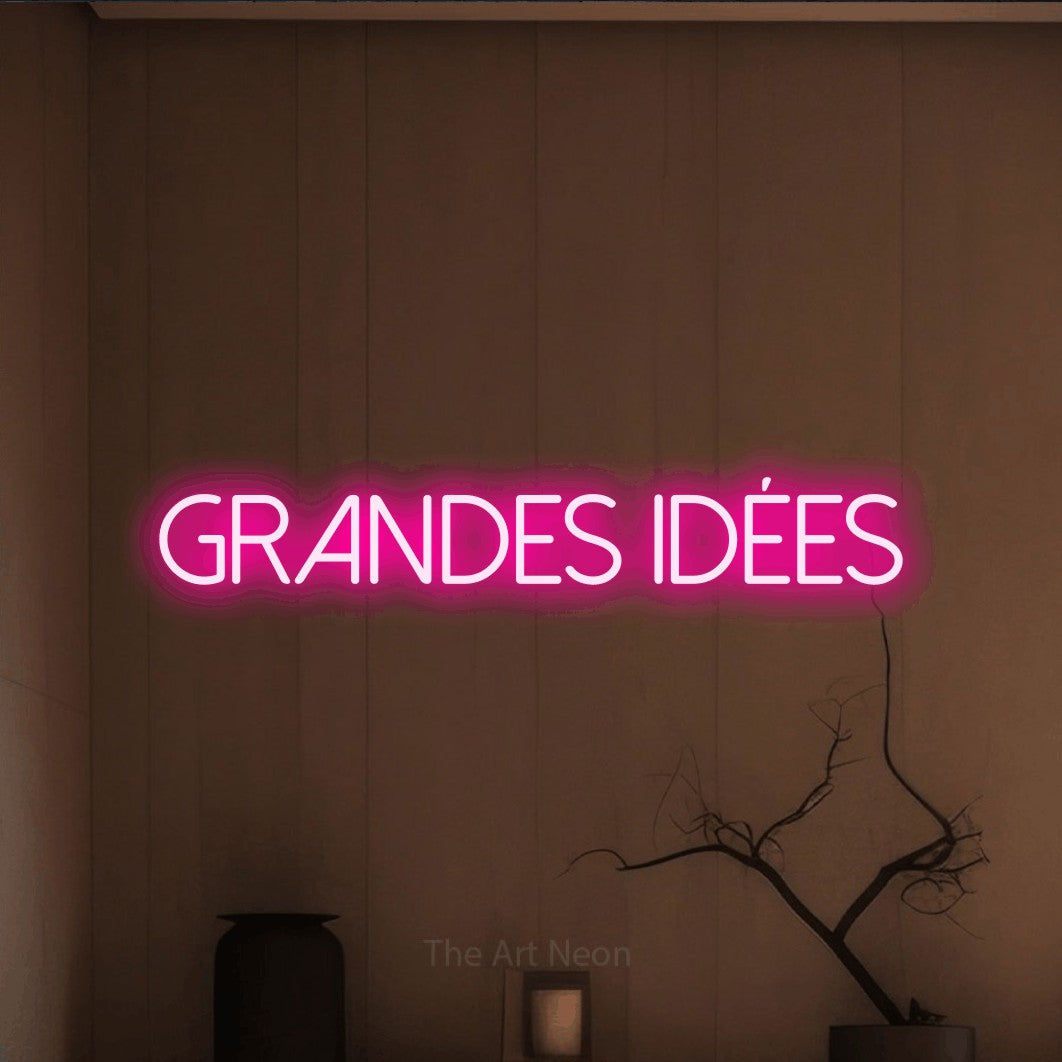 “Grandes idées” LED neon sign in hot pink, with thin sans-serif lettering, shown against a simple earth-toned interior.