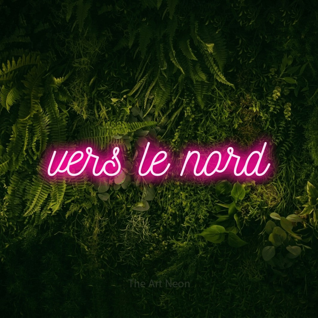 “Vers le nord” LED neon sign in hot pink, with ornate cursive lettering, shown against a dark moss and forest backdrop.