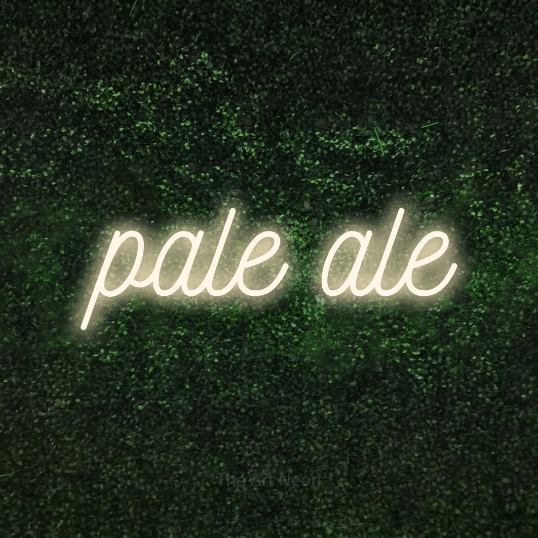 “Pale ale” LED neon sign in warm white, with ornate cursive lettering, shown against a textured green hedge.