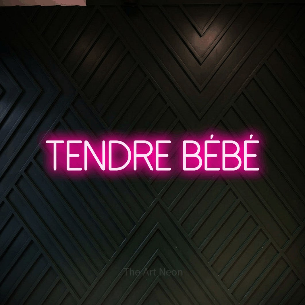 Lettrage en néon LED « Tendre bébé » en rose vif, en lettres fines sans empattement, présenté sur un mur en bois noir à motif chevron, pour une fête prénatale.