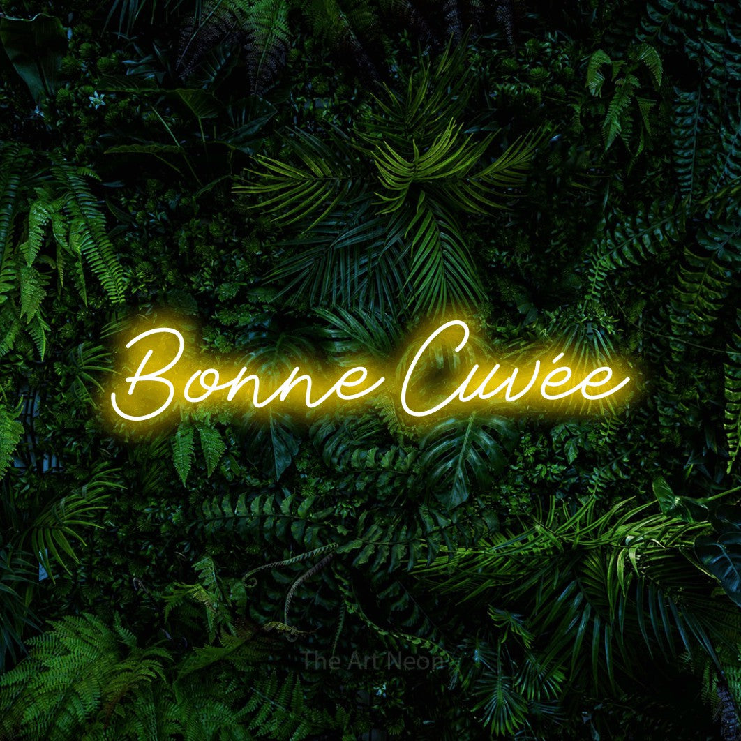 “Bonne cuvée” LED neon sign in yellow, with cursive lettering, shown against dense tropical foliage.