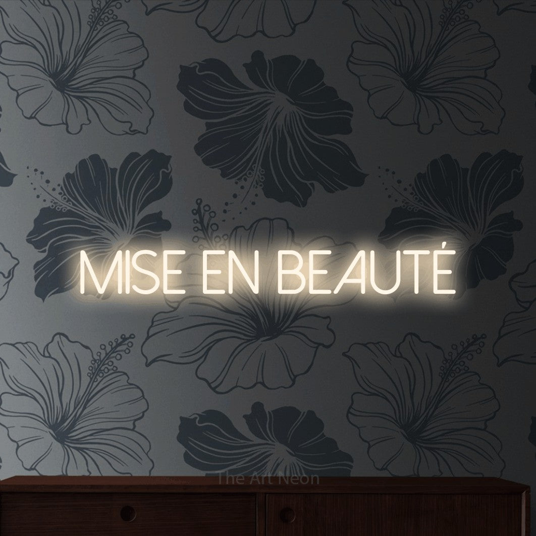 Décoration murale en néon LED « Mise en beauté » en blanc chaud, en lettres fines sans empattement, installée sur un mur gris à motifs floraux, pour un salon de beauté.