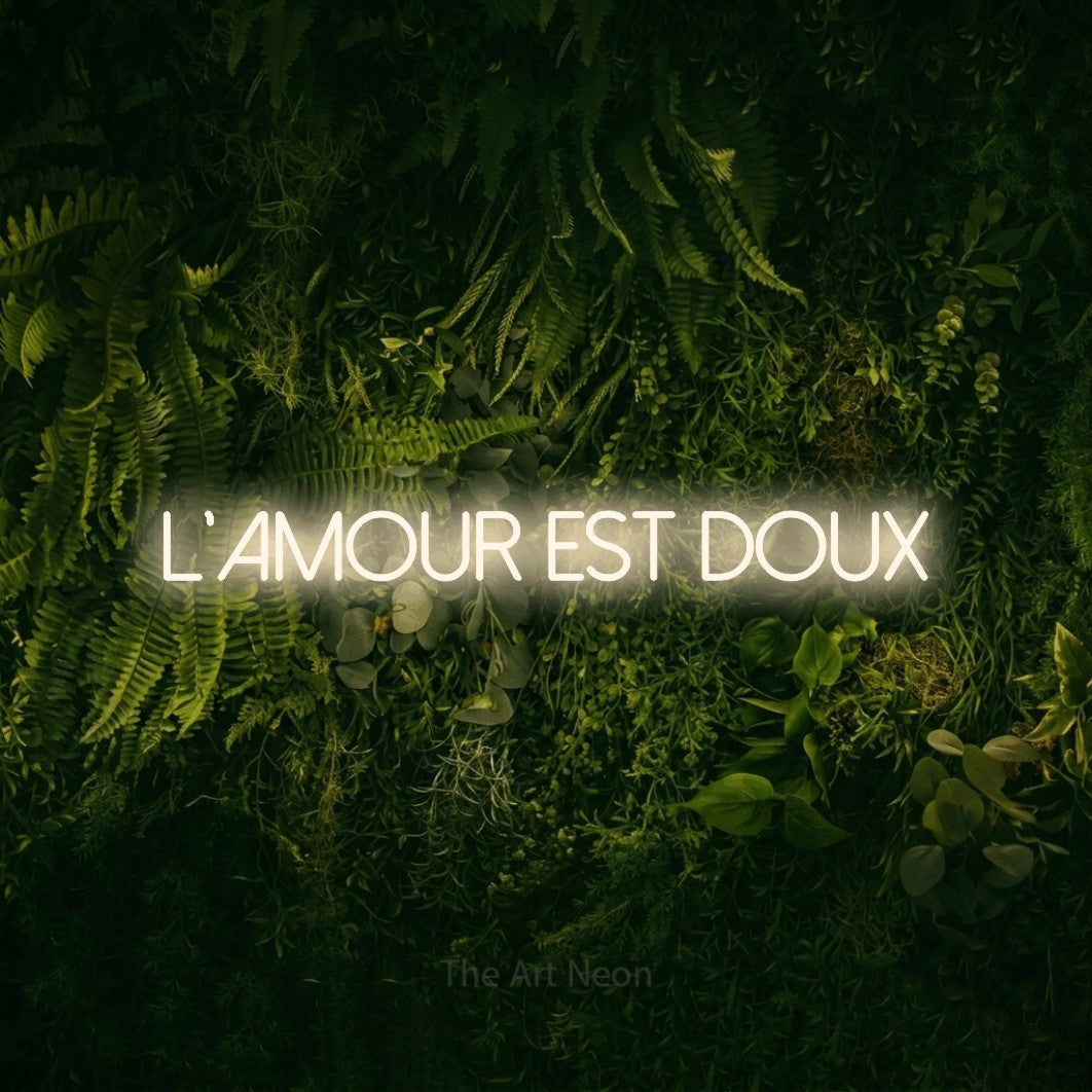 Décoration murale en néon LED « L'amour est doux » en blanc chaud, en lettres fines sans empattement, installée sur un fond sombre de mousse et de forêt, pour une réception de mariage.