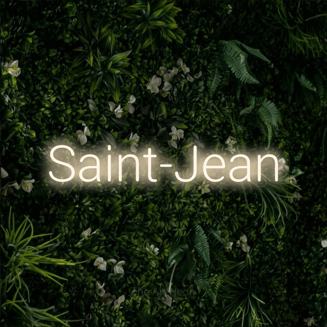 “Saint-Jean” LED neon sign in warm white, with rounded sans-serif lettering, shown against a dense green plant wall.