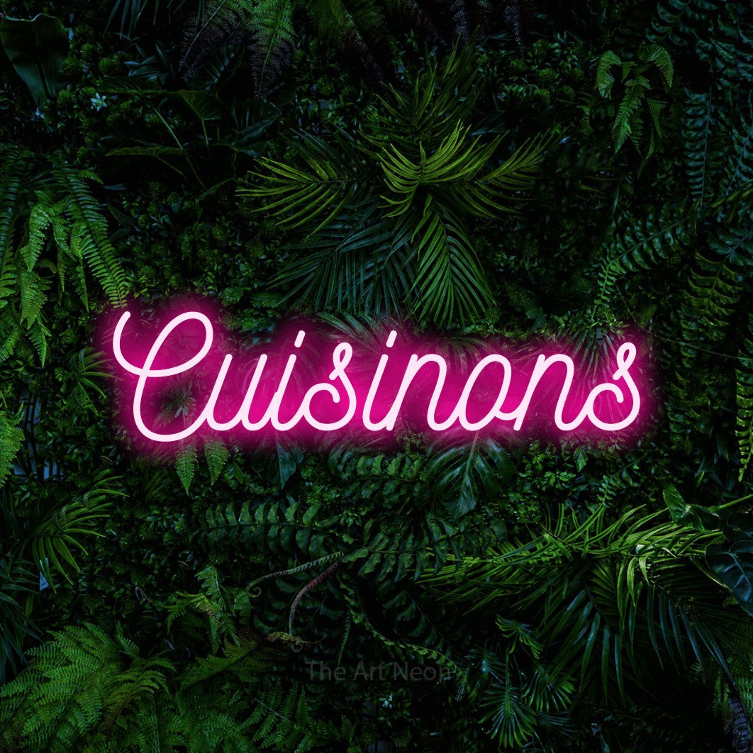 “Cuisinons” LED neon sign in hot pink, with ornate cursive lettering, shown against dense tropical foliage.