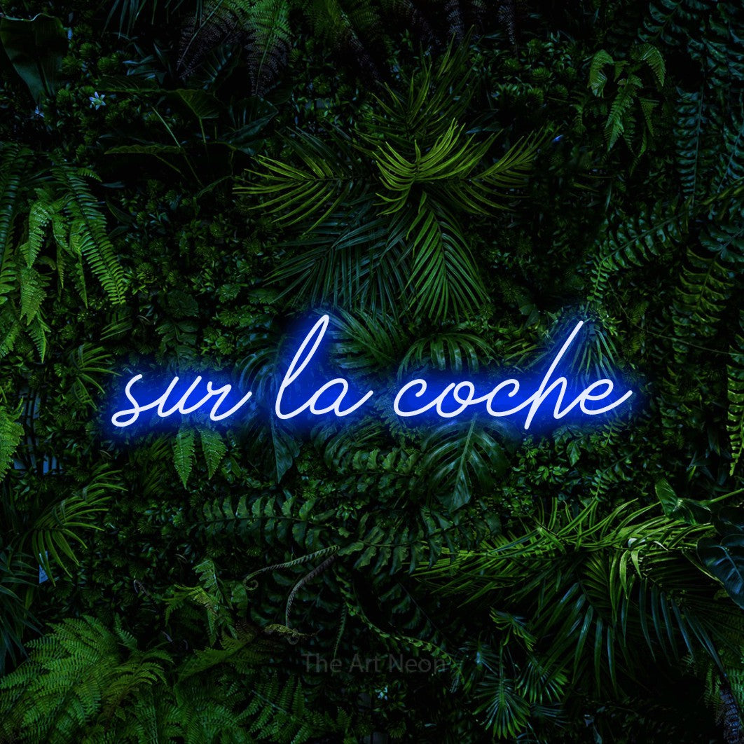 “Sur la coche” LED neon sign in blue, with cursive lettering, shown against dense tropical foliage.