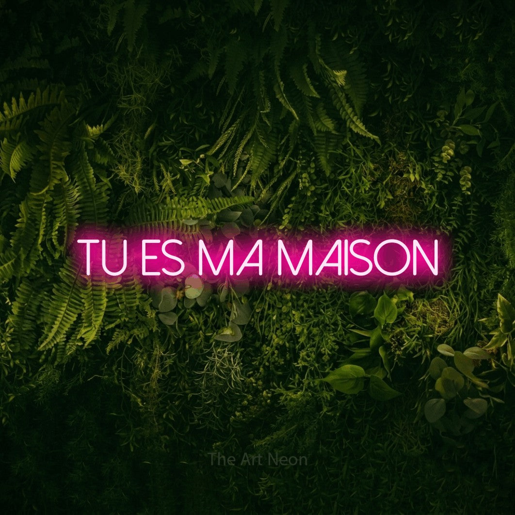 “Tu es ma maison” LED neon sign in hot pink, with thin sans-serif lettering, shown against a dark moss and forest backdrop.
