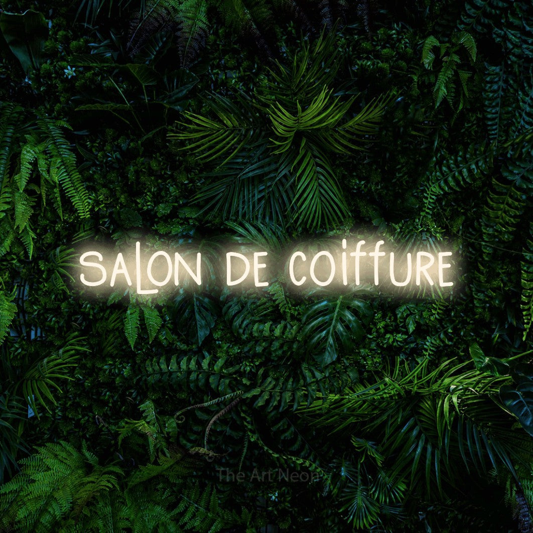 Décoration murale en néon LED « Salon de coiffure » en blanc chaud, en lettres étroites dessinées à la main, installée devant un feuillage tropical dense, pour un salon de beauté.