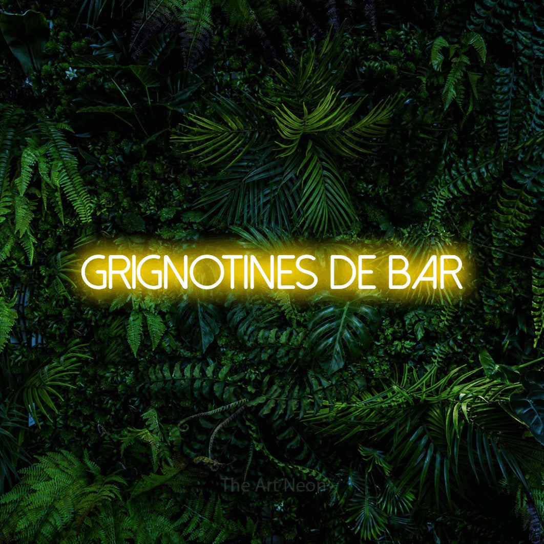 “Grignotines de bar” LED neon sign in yellow, with thin sans-serif lettering, shown against dense tropical foliage.