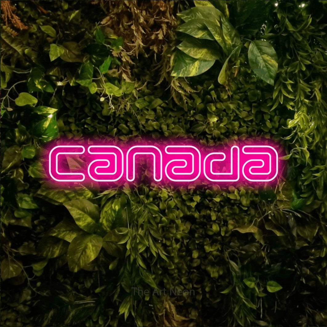 “Canada” LED neon sign in hot pink, with futuristic double-line lettering, shown against bright green and yellow foliage.