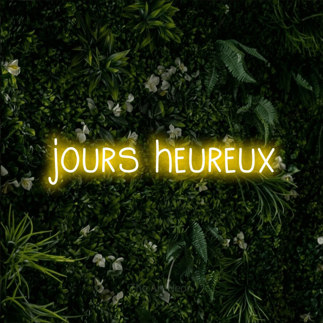 Aperçu d’une enseigne néon LED « Jours heureux » en jaune, en lettres étroites dessinées à la main, photographiée sur un mur végétal vert et dense, pour un salon.