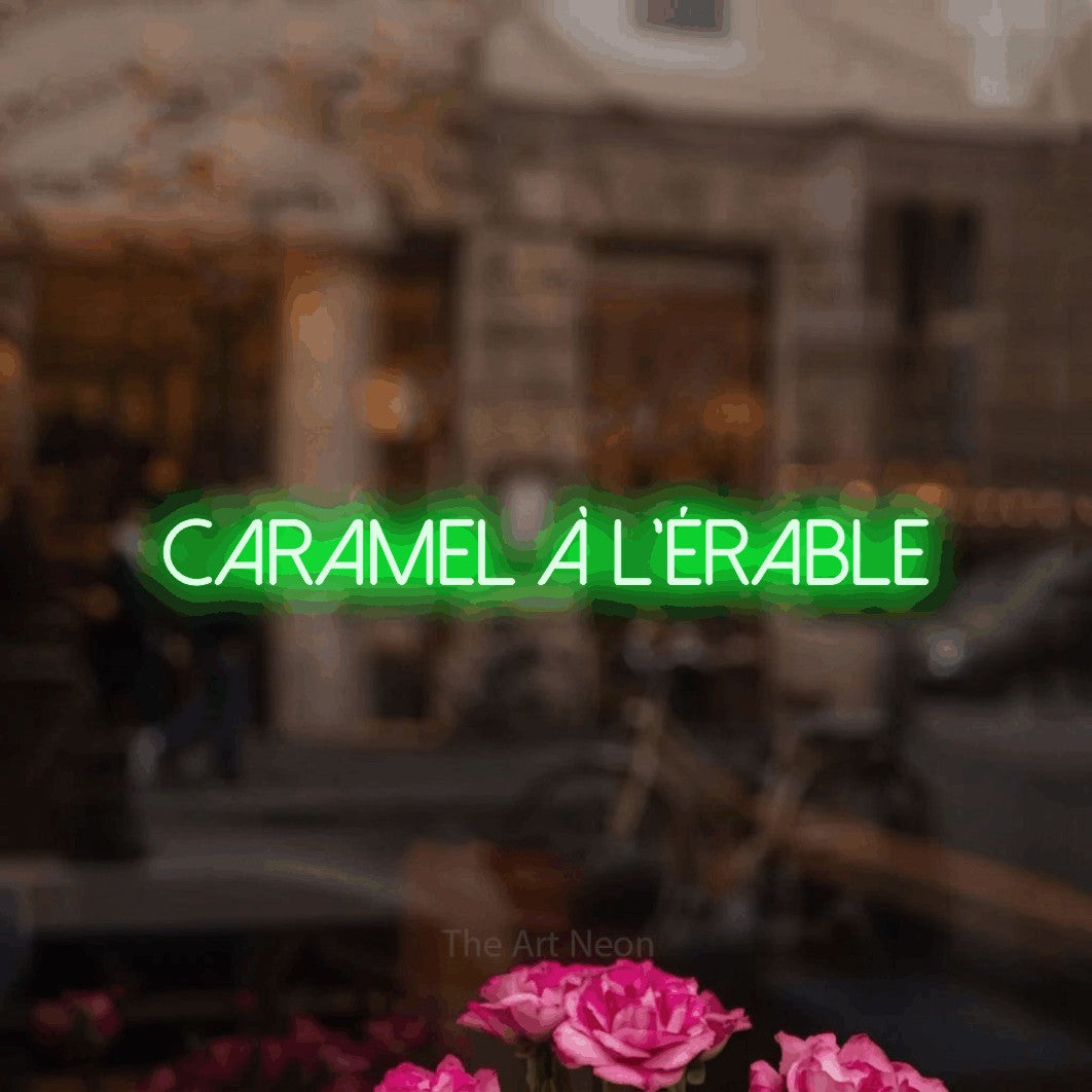 “Caramel à l'érable” LED neon sign in green, with thin sans-serif lettering, shown against a blurred café-bar interior.