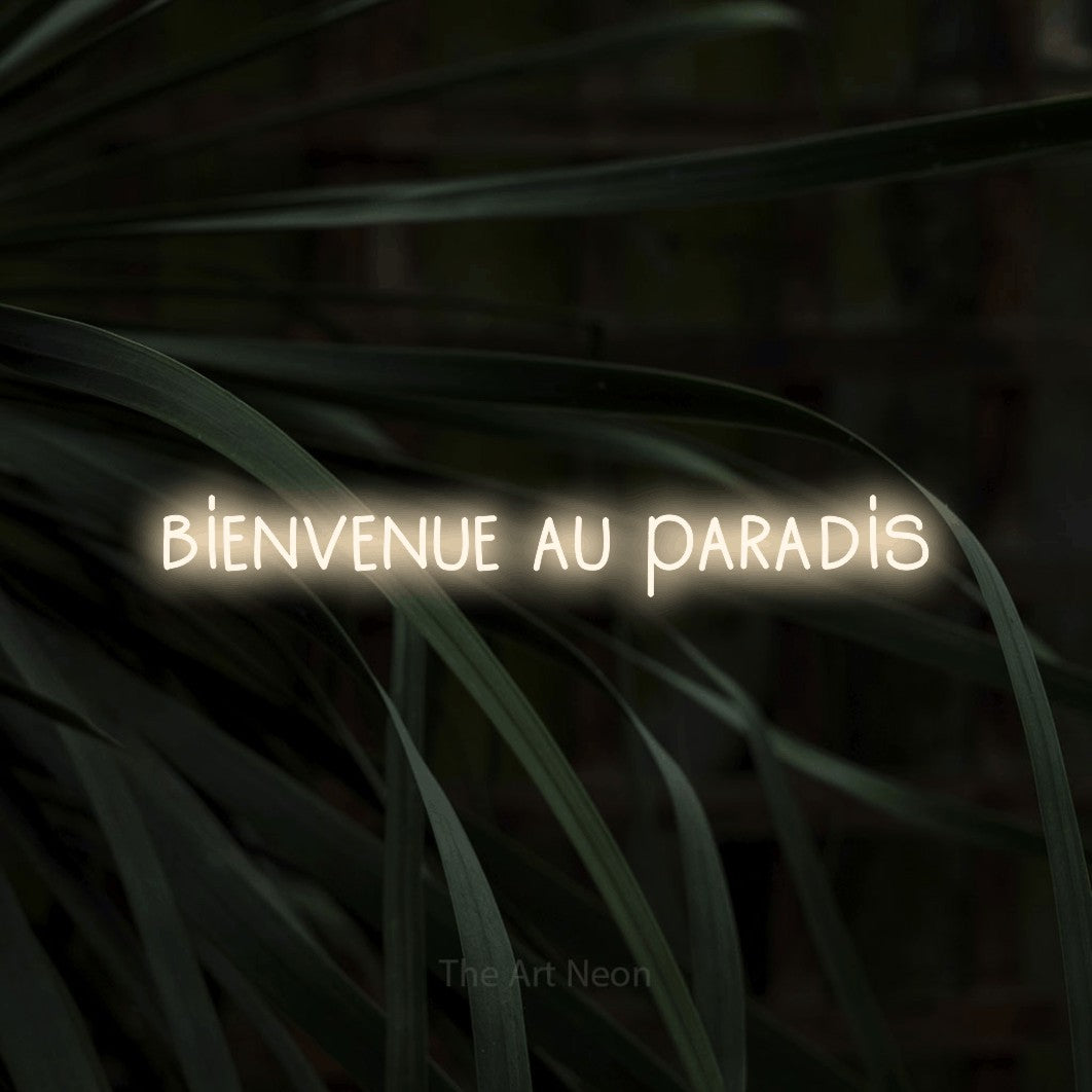 Enseigne néon LED « Bienvenue au paradis » en blanc chaud, en lettres étroites dessinées à la main, présentée sur un feuillage sombre en gros plan, pour un hôtel.
