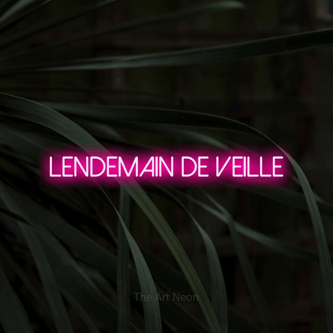 “Lendemain de veille” LED neon sign in hot pink, with thin sans-serif lettering, shown against a close-up of dark foliage.