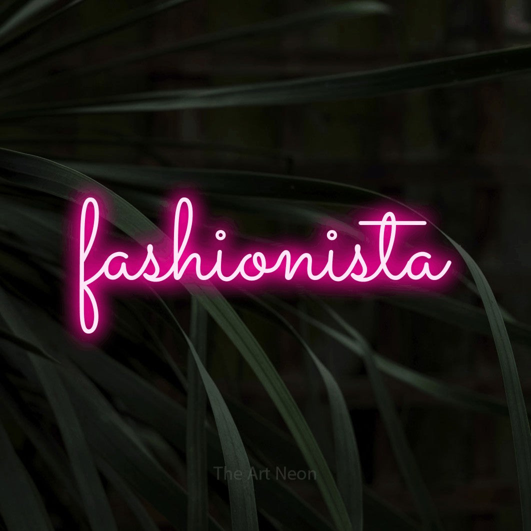 “Fashionista” LED neon sign in hot pink, with looped cursive lettering, shown against a close-up of dark foliage.
