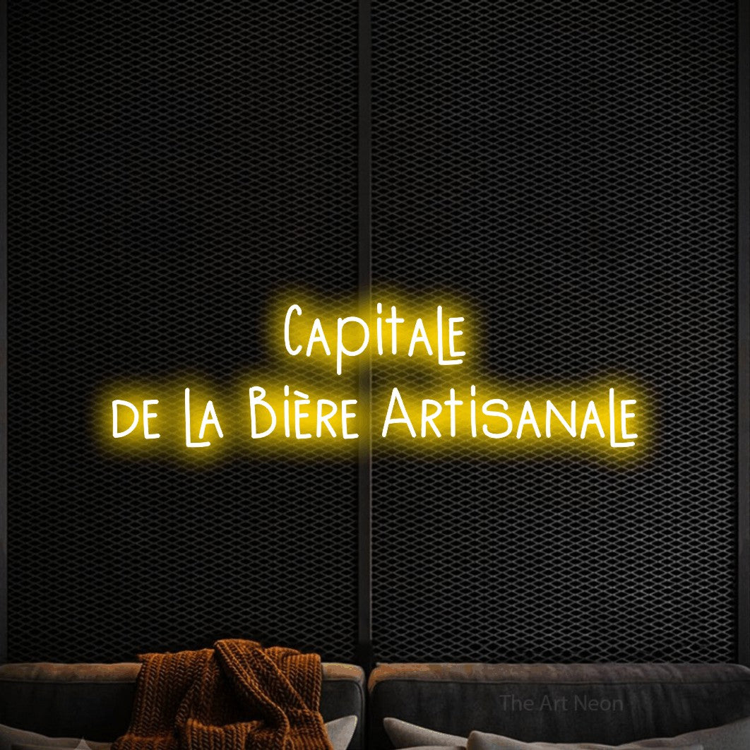 “Capitale de la bière artisanale” LED neon sign in yellow, with narrow hand-drawn lettering across 2 lines, shown against a modern dark-toned seating area.