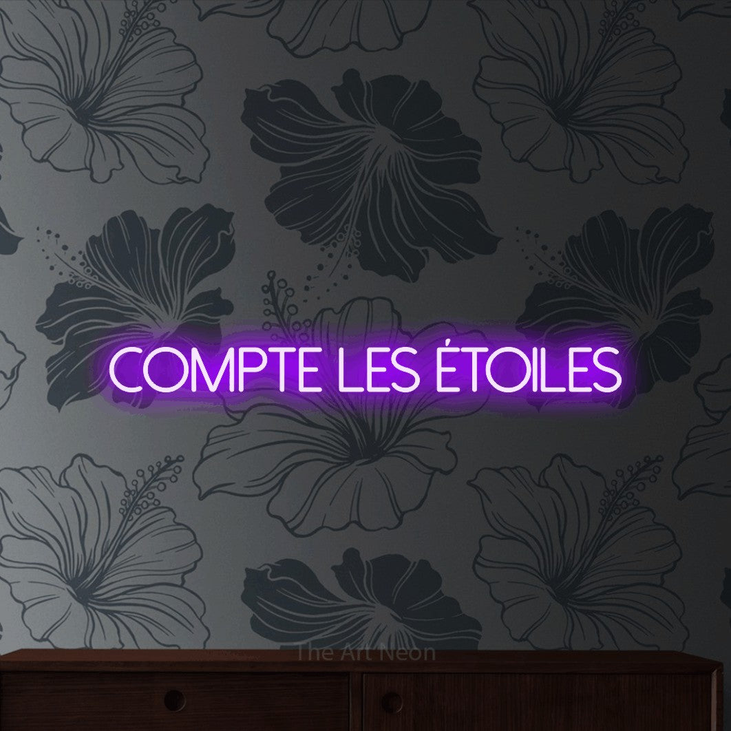 “Compte les étoiles” LED neon sign in purple, with thin sans-serif lettering, shown against a grey floral-patterned wall.
