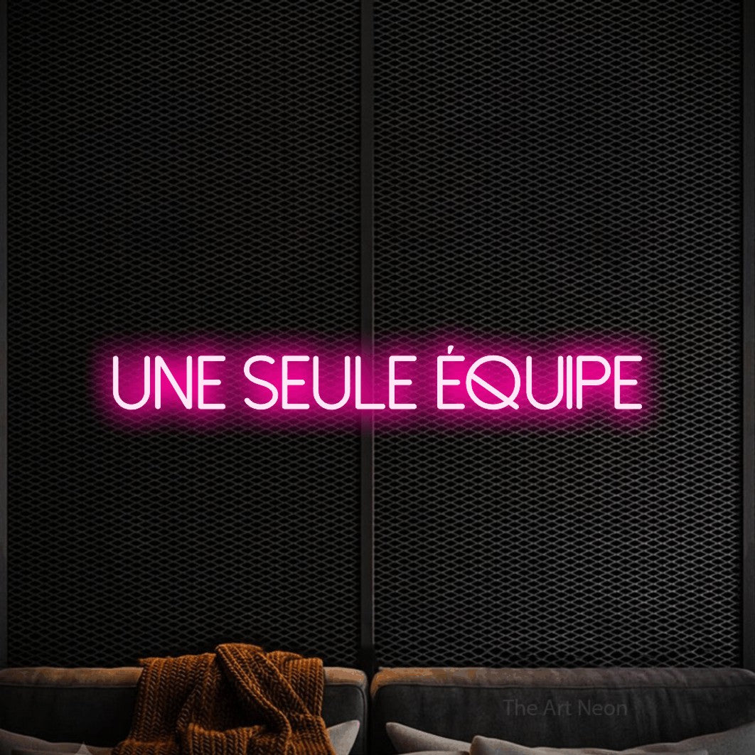 “Une seule équipe” LED neon sign in hot pink, with thin sans-serif lettering, shown against a modern dark-toned seating area.