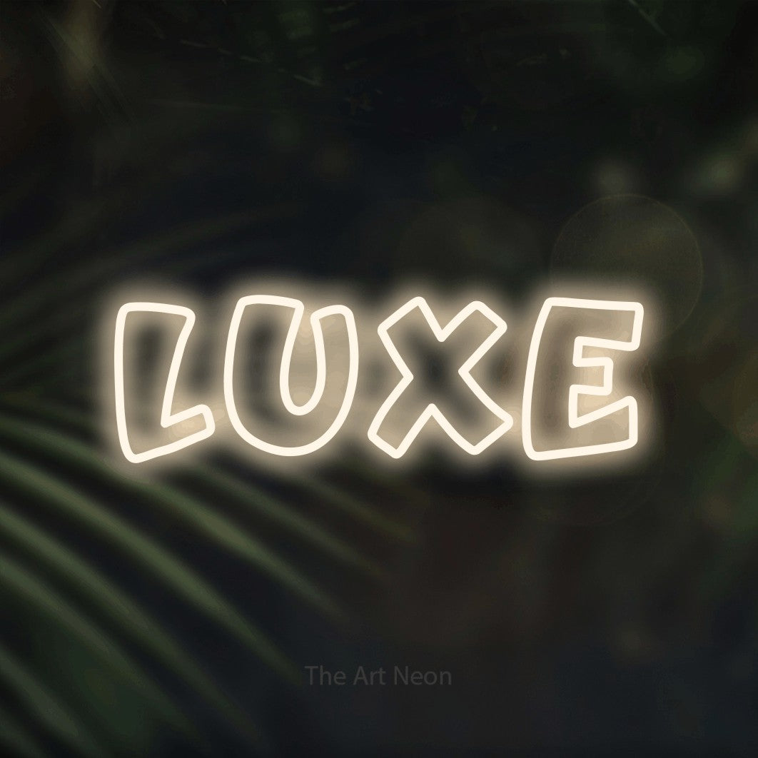 “Luxe” LED neon sign in warm white, with rounded outline lettering, shown against a blurred palm and bokeh-light backdrop.