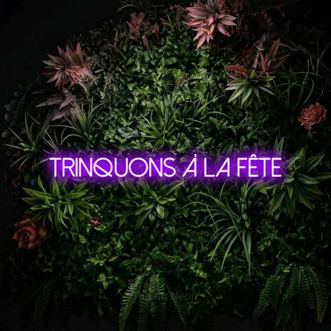 “Trinquons à la fête” LED neon sign in purple, with thin sans-serif lettering, shown against a flowering plant wall.